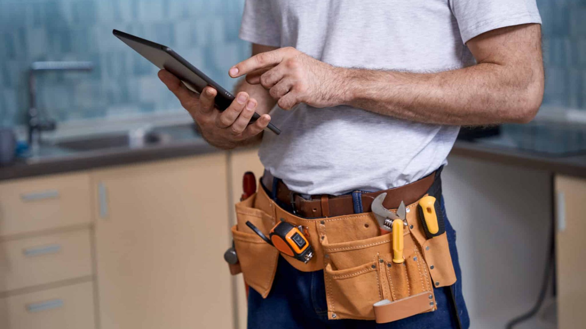 Young builder working with finger on digital tablet on kitchen background. Home master concept, construction and repair